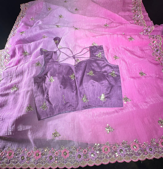 A pink and purple traditional Indian outfit set, featuring a sheer pink dupatta with floral embroidery and mirror work, a matching purple blouse with tie-back straps, and a purple skirt, laid out on a dark surface.